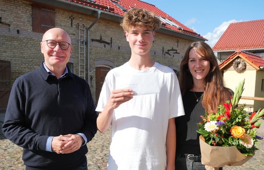 Drei Menschen stehen nebeneinander, die Frau rechts hält einen Blumenstrauß